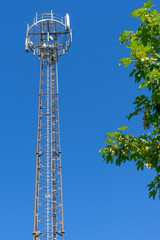 Mobilfunkantenne (Handymast) mit Baum vor blauem Hintergrund (Himmel)