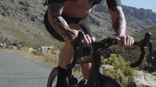 Close up of strong and muscular man cycling on mountain highway road. Focus on muscular hands of professional cyclist riding over countryside hill roads.
