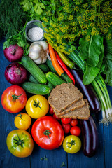 Assorted vegetables on a dark wooden background with slices of bread and salt