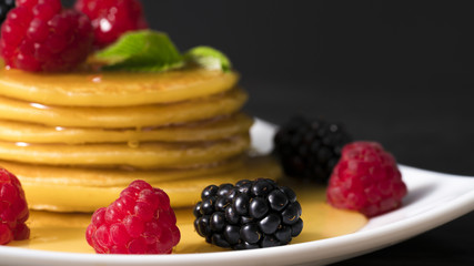 pancakes with honey raspberries and blackberries on a black wooden background