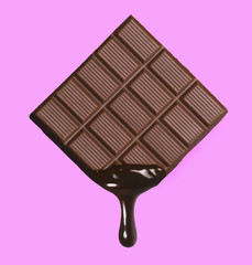 Dark chocolate bar and melted brewing drop on pink background.
