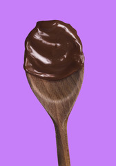 Melted dark chocolate wood spoon isolated on pink background.