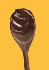 dark melted chocolate wood spoon on yellow background.