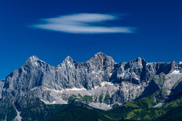 Fototapeta premium Hohe Dachstein mountain range in Austria with a soft white cloud on a deep blue sky