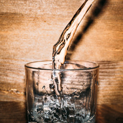 Pure fresh water is pouring into glass on wooden background close up, healthy drink