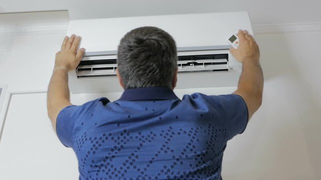 The man stands under the running air-conditioner and cools