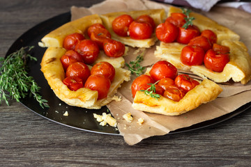 Homemade tart with cherry tomatoes of puff pastry with raw tomatoes and thyme on  dark wooden background. Tomatoes tart tatin. Rustic style.