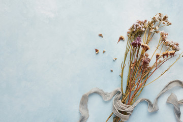 Flat lay concept of feminine light blue background with dried wildflowers tied with silk. Top view...