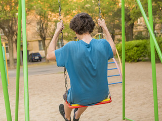 back view of teenager boy swinging on a playing ground
