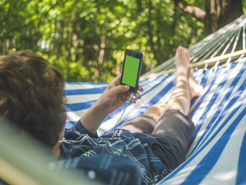 young person holding phone with green chroma key lying on a hammock