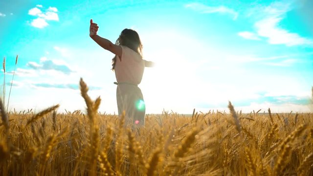 Beauty girl outdoors enjoying nature wheat field slow motion video. Beautiful girl in white dress running nature freedom happiness hands to the side on field at sunset light and lifestyle the blue sky