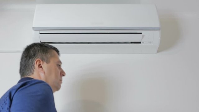 The man approaches the air conditioner and turns it on with the remote control