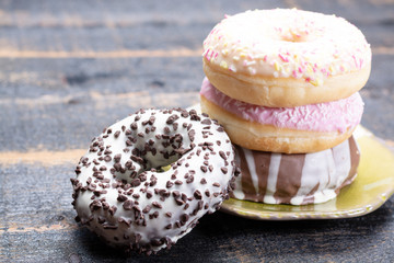 Colorful sweet glazed donuts from bakery on black wooden background close up