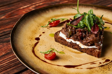 Fresh Bruschetta with lamb beef. Open sandwich with Dark rye bread, dried cherry tomatoes, rosemary, olives and arugula on plate at luxury restaurant table, top view. Delicious snack food