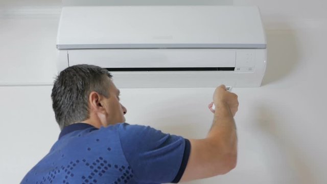 The man approaches the air conditioner and turns it on with the remote control