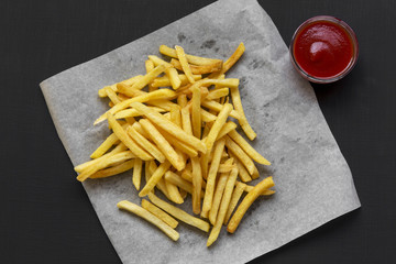 Fresh fried tasty french fries with ketchup over black background, from above. Overhead, flat lay, top view.