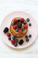Pancakes with berries and honey on a pink plate, high angle. Closeup.
