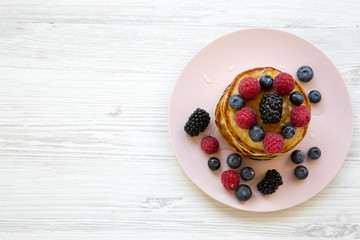Pancakes with berries and honey on a pink plate, view from above. Copy space.