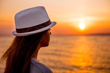 Young girl on the beach at sunset. girl in a white hat on the beach in the evening. Woman tourist looking at sunset at sea. girl on the beach, tourist near the sea, sunset in the ocean
