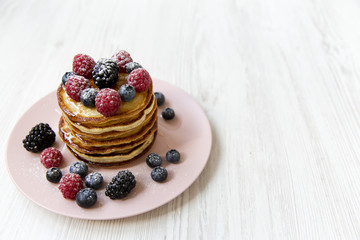 Pancakes with berries on a pink plate, high angle. Healthy summer food. Copy space and text area.
