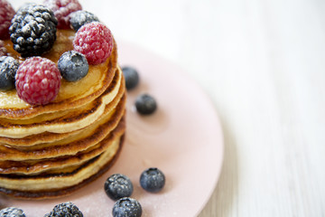 Pancakes with berries on a pink plate, side view. Healthy summer breakfast. Closeup. Copy space.