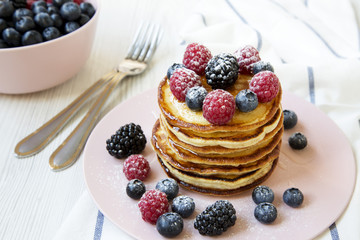 Pancakes with berries on white wooden surface, side view. Close-up.