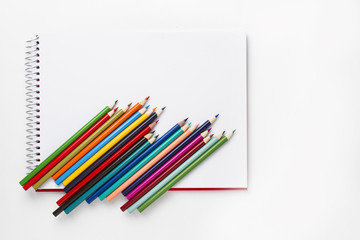 Drawing notebook and colored pencils on white table