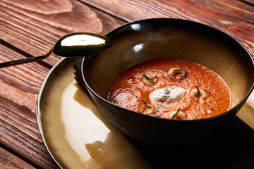 Hot Tomato soup with shrimp. Seafood creamy soup with goat cheese, olive powder, wild shrimps on bowl plate at wooden table, top view, close-up. Delicious vegetarian diet food.