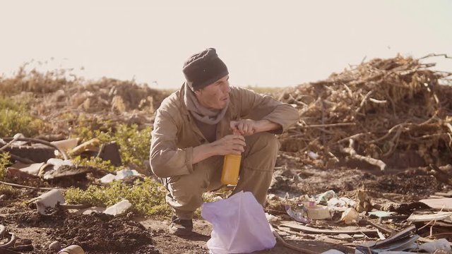 portrait of a dirty homeless man in a dump eating food looking for food in the package with walking goes looking for food slow motion video. homeless dirty man roofless person looking for food in a