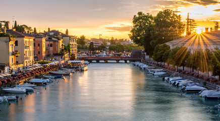 Fototapeta premium Sunset, boats and the bridge in port on Lake Garda, Peschiera del Garda