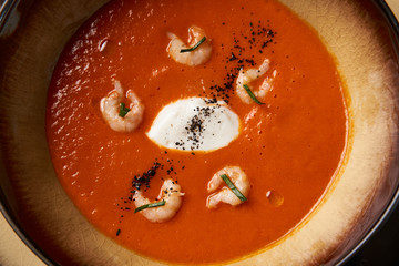 Hot Tomato soup with shrimp. Seafood creamy soup with goat cheese, olive powder, wild shrimps on bowl plate at wooden table, top view, close-up. Delicious vegetarian diet food.