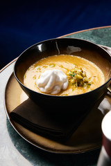 Pumpkin cream soup with cream and pumpkin seeds, coconut milk, green oil, sprouts of lentils in bowl plate on table, top view, close-up. Delicious vegetarian diet food 