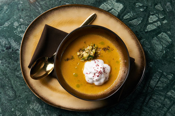 Pumpkin cream soup with cream and pumpkin seeds, coconut milk, green oil, sprouts of lentils in bowl plate on table, top view, close-up. Delicious vegetarian diet food 