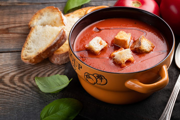 Homemade tomato soup with Basil, toast and olive oil on a wooden table. Prepared a vegetarian dish on a dark background