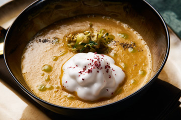 Pumpkin cream soup with cream and pumpkin seeds, coconut milk, green oil, sprouts of lentils in bowl plate on table, top view, close-up. Delicious vegetarian diet food 