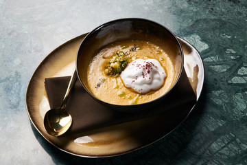 Pumpkin cream soup with cream and pumpkin seeds, coconut milk, green oil, sprouts of lentils in bowl plate on table, top view, close-up. Delicious vegetarian diet food 