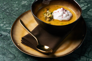 Hot Pumpkin cream soup with cream and pumpkin seeds, coconut milk, green oil, sprouts of lentils in bowl plate on table, top view, close-up. Delicious vegetarian diet food 