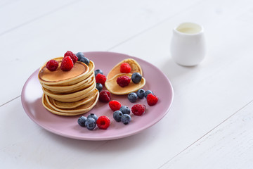 Homemade delicious pancakes with fresh berries in a violet plate on a white background. A tasty and healthy breakfast of pancakes with raspberries, blueberries and fresh milk.