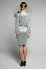 Back view of unrecognizable blonde woman wearing elegant cocktail dress of silver color and black high heels. Isolate on white background.