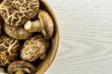 Fresh raw brown shiitake mushroom in a wooden bowl flatlay isolated on grey wood.