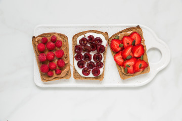 Healthy breakfast toasts with peanut butter, soft cheese, cherries, strawberries, raspberries, chia and pumpkin seeds
