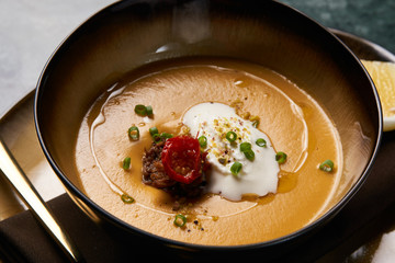 Hot Lentil cream soup with baked lamb, cream fresh and spearmint. Delicious healthy soup food in bowl plate on table background, close-up, top view