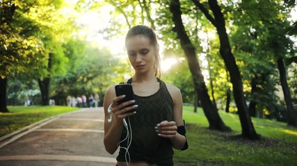 Beautiful woman use smartphone in park sunshine slow motion sun outdoor health hand girl tree sport fitness summer nature internet technology runner exercise phone workout young mobile cellphone