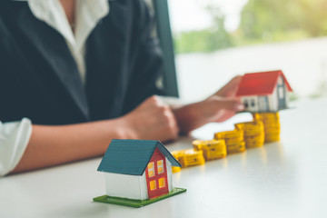 Women Real Estate Agent hold a small house model in her hand and gold coin stack, Real estate Concept