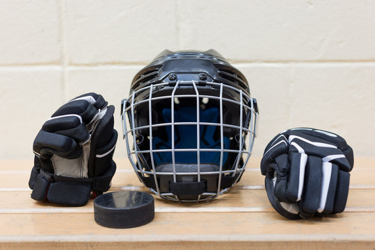 Photo Of  Kid's Hockey Equipment: Glows, Helmet And Puck. The Gear Are On The Bench