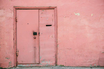 Old pink door with combination lock on unideal peeling wall of aged building. Retro background of entrance in vintage house. Unusual imperfect rough construction. Habitable grunge glamour home.