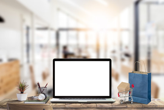 Mock Up Blank Screen Of Laptop With Small Shopping Cart And Shopping Paper Bag On Wooden Table