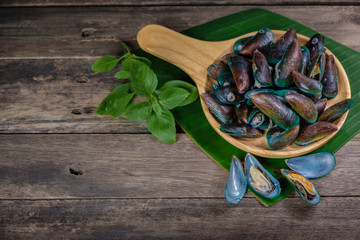 mussels in a wooden dish There is a banana leaf below.