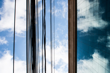 Clouds are reflected on the glass windows of a corporate modern building and electric wires can be seen in front of it.
