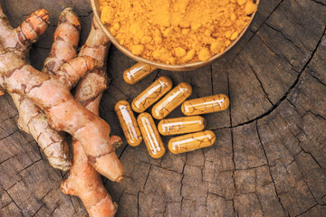 Turmeric powder in wooden bowls and turmeric capsules on wooden background